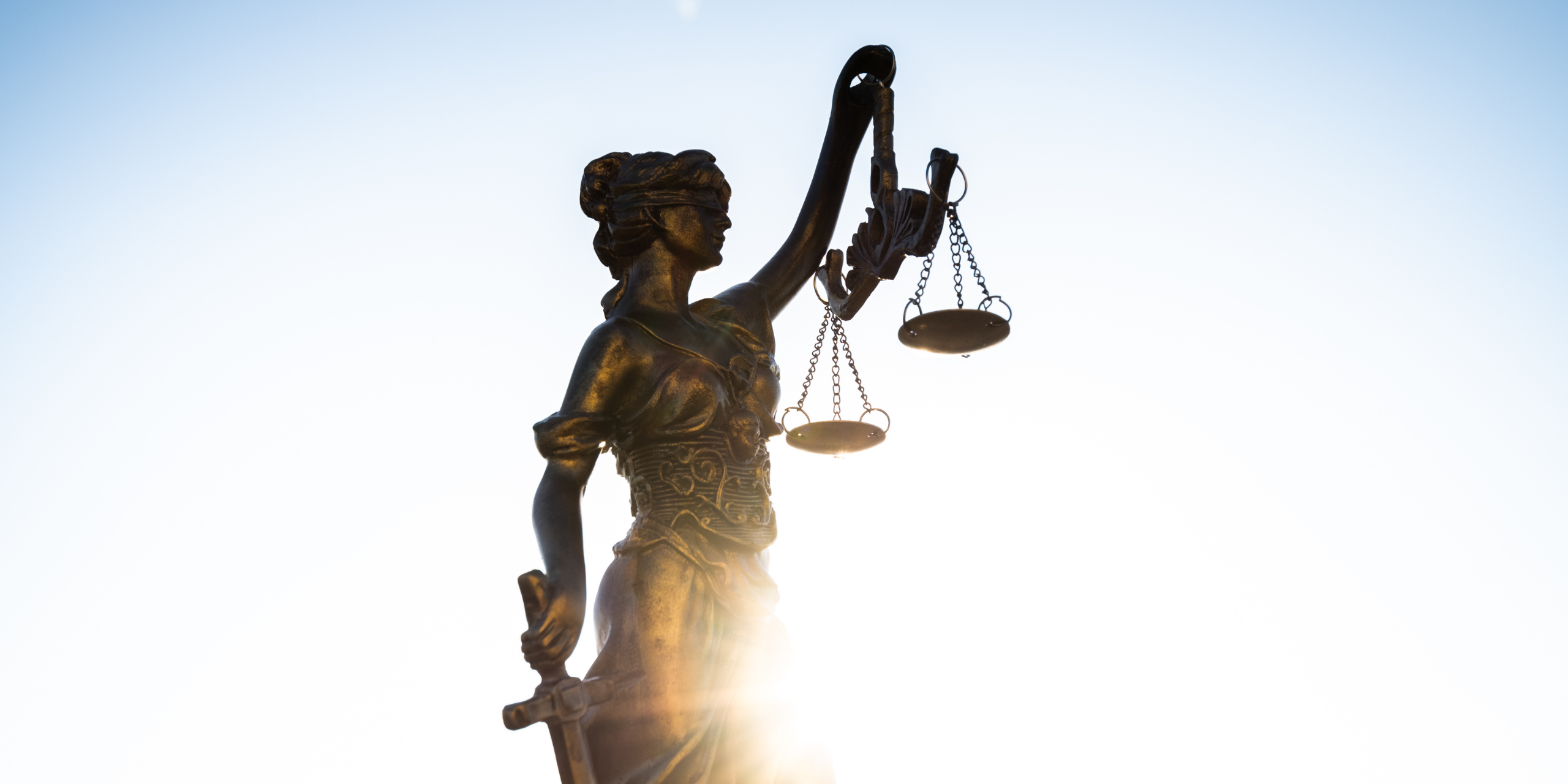 A statue of Lady Justice with the sun coming up behind it.
