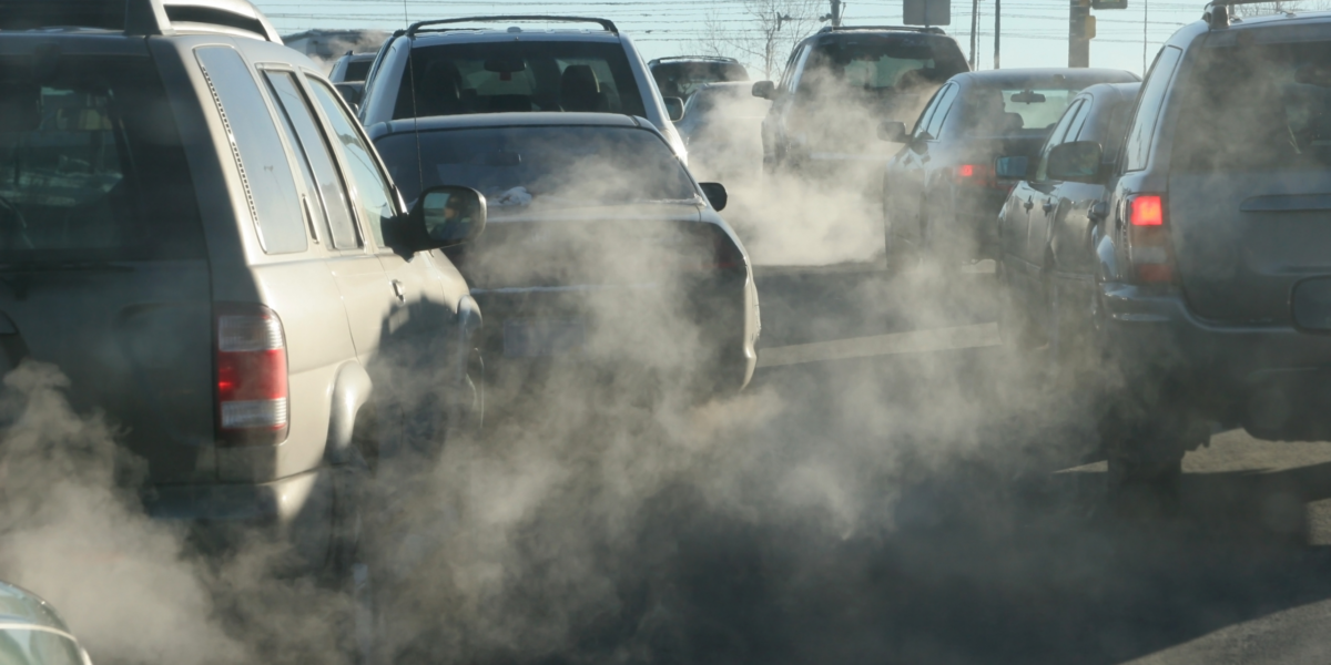 Cars stopped at an intersection, exhaust coming from all of their tailpipes.